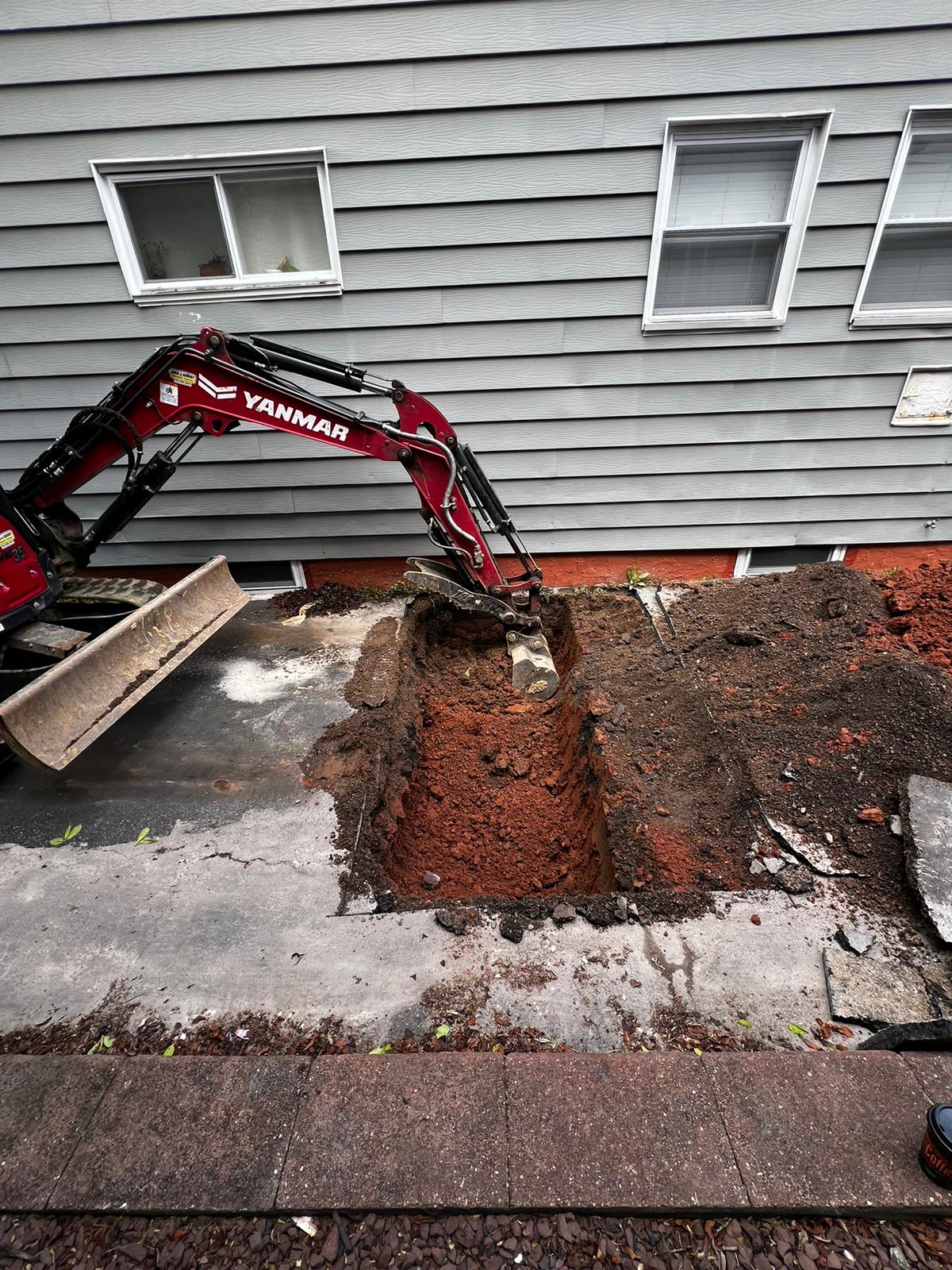 Mini excavator digging out a sewer line beside a home