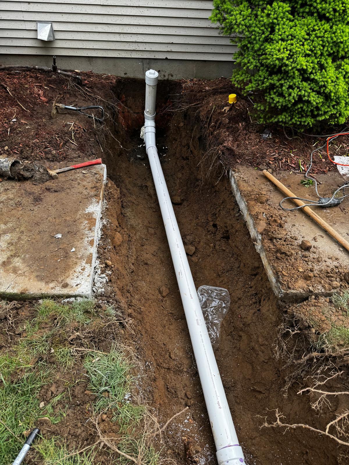 New PVC drain line laid in an open trench alongside a house foundation